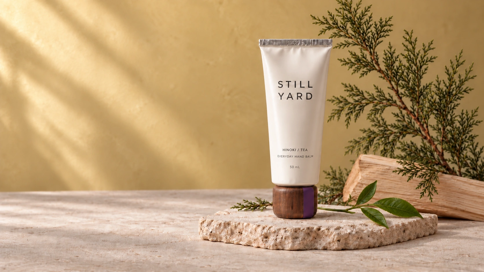 Still Yard Hinoki / Tea hand balm with a walnut cap, arranged with its botanical ingredients on pale stone