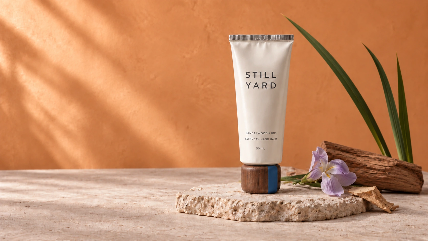 Still Yard Sandalwood / Iris hand balm with a walnut cap, arranged with its botanical ingredients on pale stone