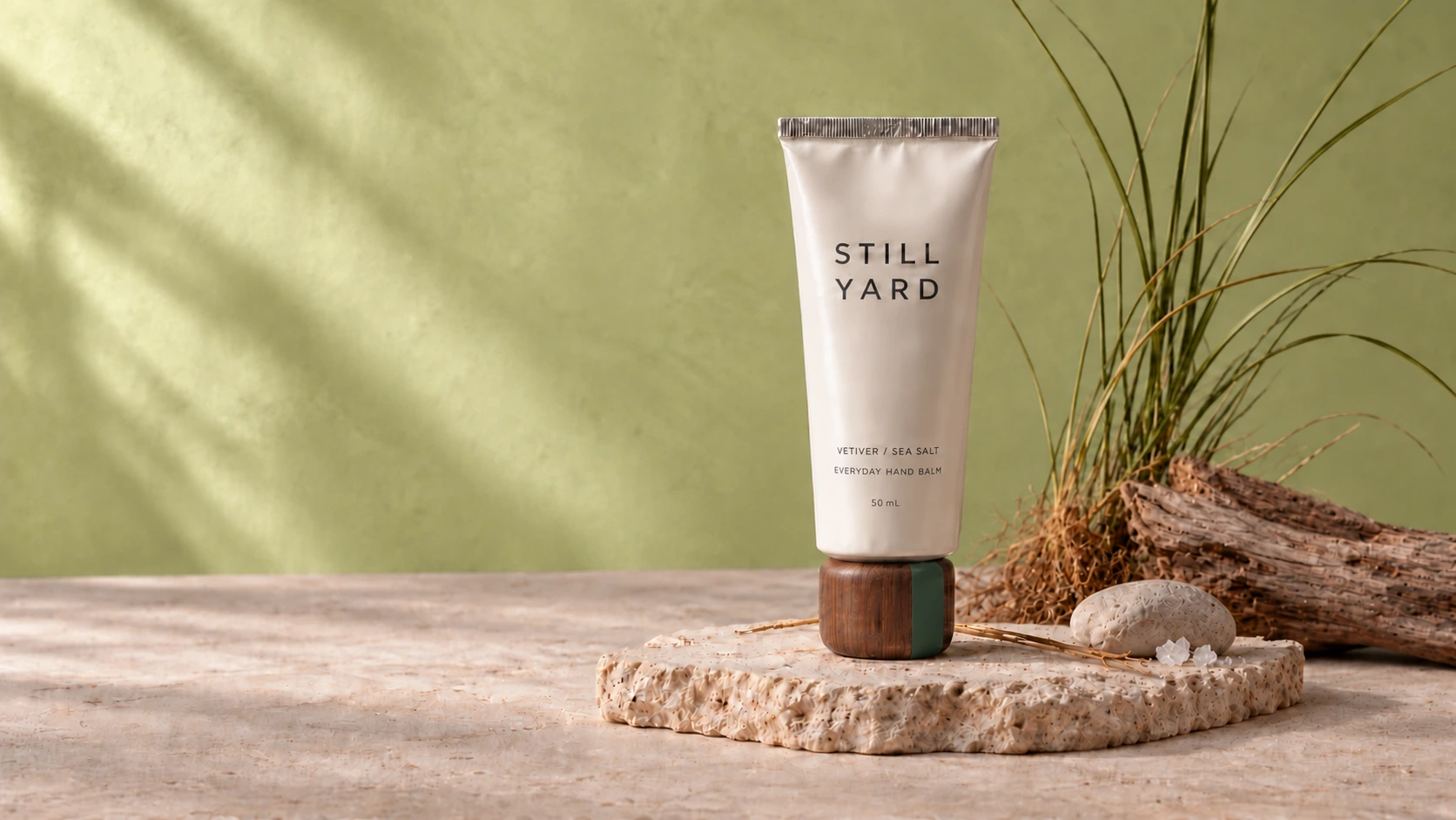 Still Yard Vetiver / Sea Salt hand balm with a walnut cap, arranged with its botanical ingredients on pale stone